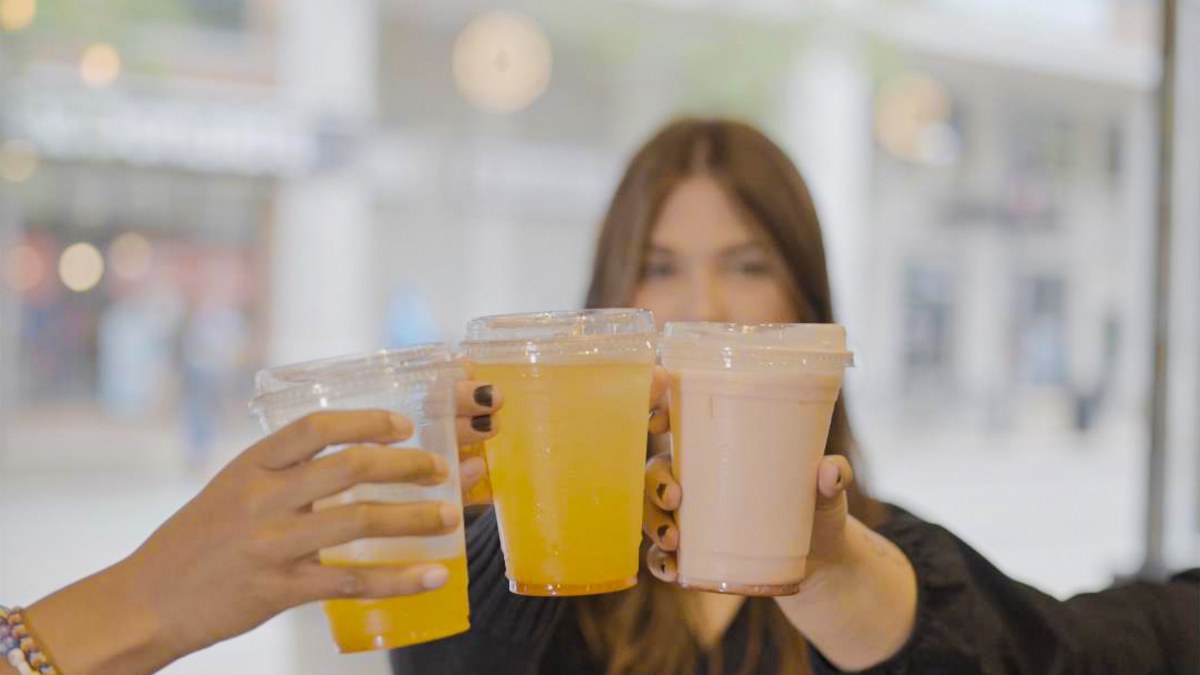 Three customers touching their cups together in front of the storefront window, a fourth person smiling behind them